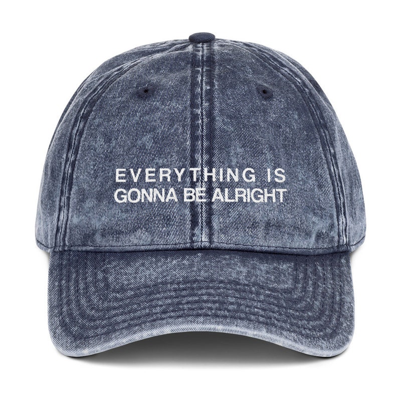 May include: A blue denim baseball cap with the text "EVERYTHING IS GONNA BE ALRIGHT" embroidered in white on the front.