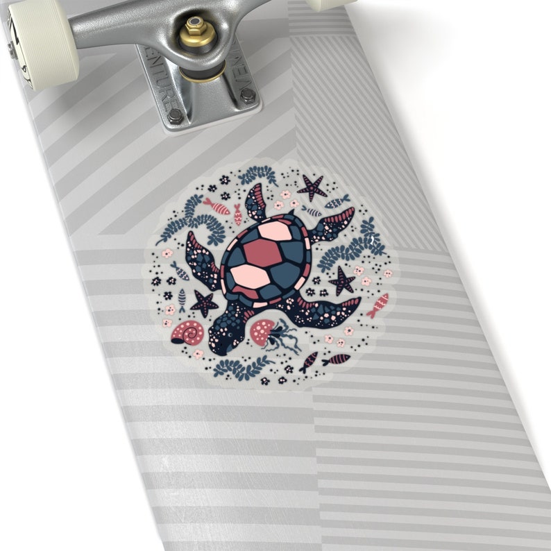 May include: A gray and white skateboard with a circular sticker featuring a pink and blue sea turtle surrounded by sea life, including starfish, seashells, and fish.