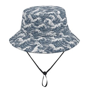 May include: A navy and white bucket hat with a repeating wave design. The hat has a black adjustable chin strap. This hat is a stylish accessory for sun protection.