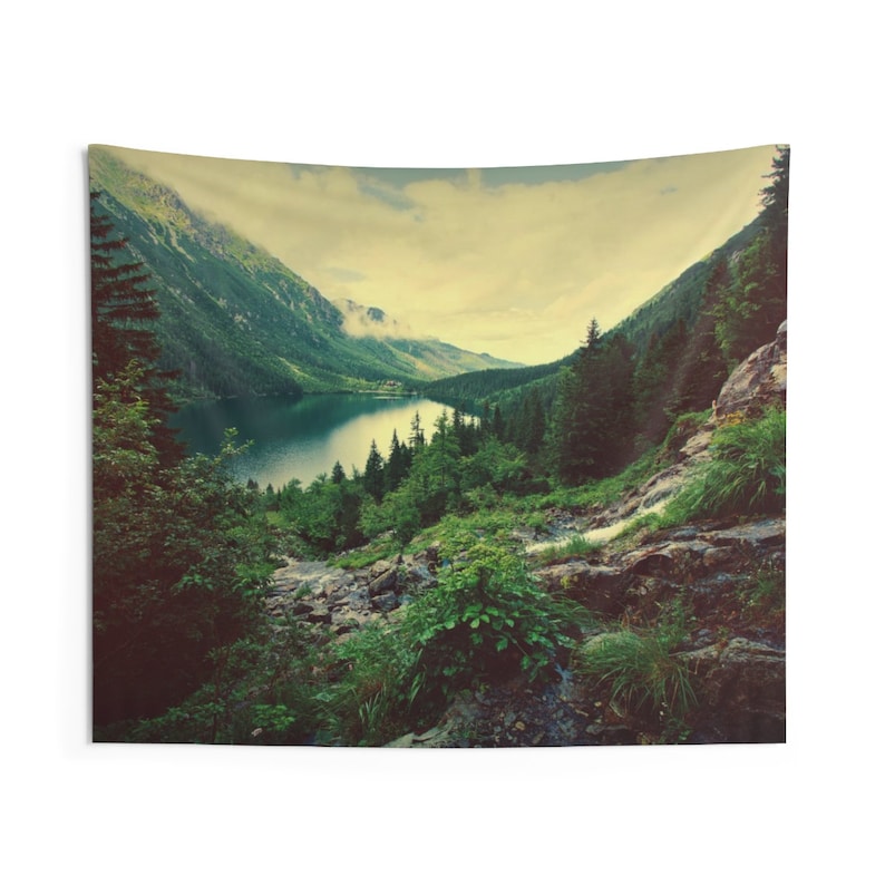May include: A scenic tapestry featuring a mountain lake surrounded by lush green trees and a rocky hillside. The sky is a soft yellow with a hint of blue, creating a tranquil and serene atmosphere.