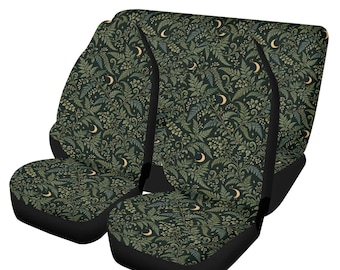 May include: A pair of car seat covers featuring a dark green background with a repeating pattern of ferns, small flowers, and crescent moons in shades of light green, cream, and gold. The covers have black side panels and black straps.