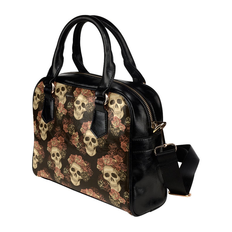 May include: Black leather handbag with a skull and rose print. The bag has a top zipper closure, two top handles, and a detachable shoulder strap.
