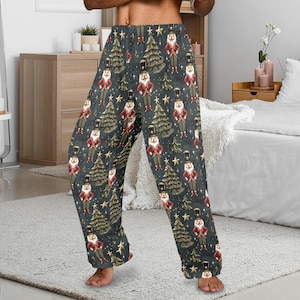 May include: Dark gray pajama pants with a repeating pattern of nutcrackers, Christmas trees, and stars. The nutcrackers are dressed in red and black uniforms. The trees are gold, and the stars are yellow. The pants are made of a soft, flowing fabric.