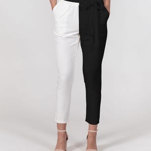 May include: Black and white color block pants with a high waist and a tie belt. The pants have a straight leg and pockets. The model is wearing nude heels. The pants are split down the middle with one side white and the other black.