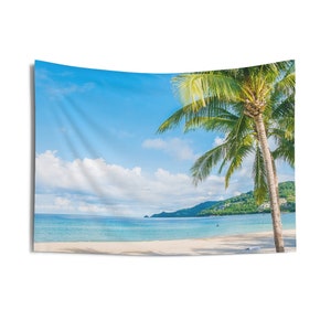 May include: A tropical beach scene with a white sandy beach, clear blue water, and a lush green palm tree in the foreground. The sky is a bright blue with fluffy white clouds.