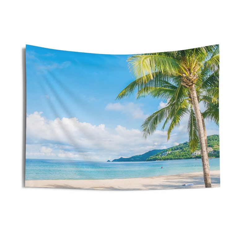 May include: A tropical beach scene with a white sandy beach, clear blue water, and a lush green palm tree in the foreground. The sky is a bright blue with fluffy white clouds.