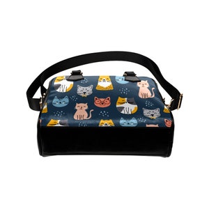 May include: A black leather handbag with a blue and white pattern of cats. The cats are in various poses and colors, including orange, yellow, pink, and blue.