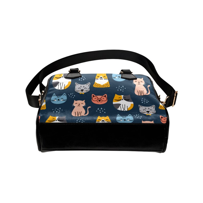 May include: A black leather handbag with a blue and white pattern of cats. The cats are in various poses and colors, including orange, yellow, pink, and blue.
