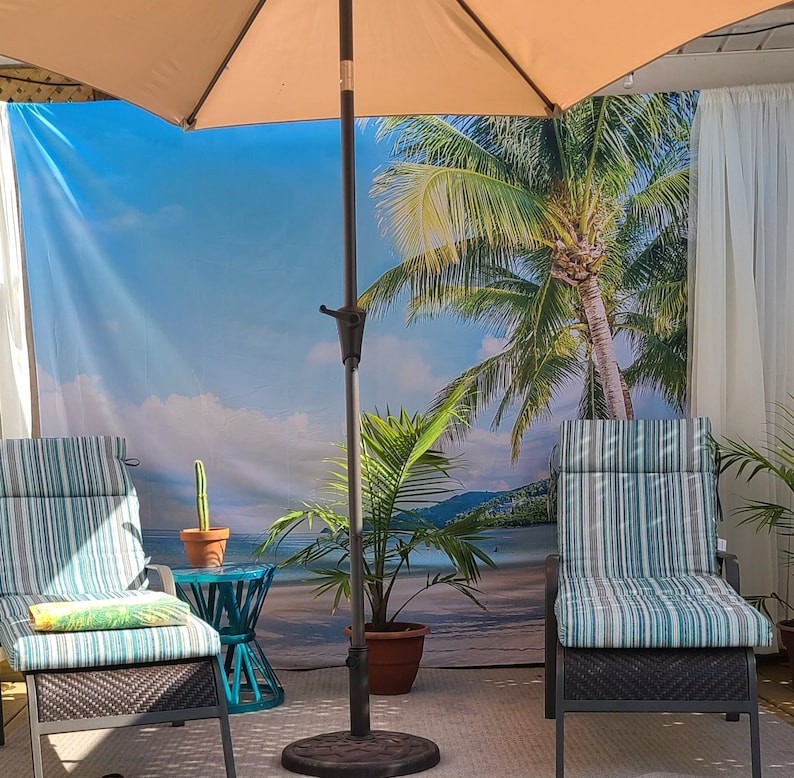 May include: Two striped patio chairs with a tropical beach scene backdrop. A brown umbrella with a white canopy provides shade. A small potted plant sits in front of the chairs.