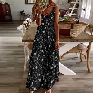 May include: A black maxi dress with a floral pattern. The dress features a V-neckline and spaghetti straps. The white floral design is spread across the dress. The dress is floor-length and suitable for casual wear.
