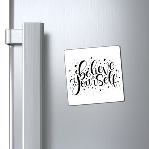 May include: White square magnet with black lettering that reads "Believe in yourself" with small black stars scattered around the text.