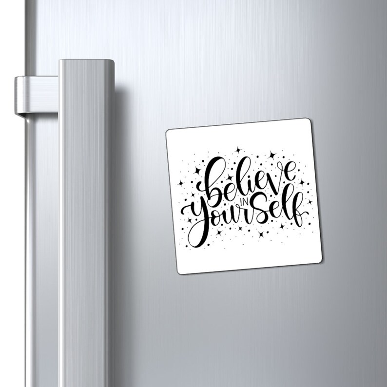 May include: White square magnet with black lettering that reads "Believe in yourself" with small black stars scattered around the text.