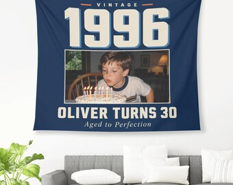 May include: A navy blue wall tapestry featuring the text VINTAGE 1996 at the top and OLIVER TURNS 30 Aged to Perfection at the bottom. The center displays a photograph of a child blowing out candles on a birthday cake.