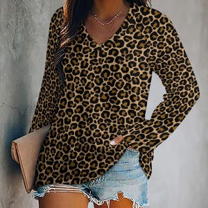 Puede incluir: Una blusa de manga larga con cuello en V y estampado de leopardo en tonos marrón y negro. La blusa se combina con pantalones cortos de mezclilla. La blusa tiene un corte holgado y está hecha de un material suave.