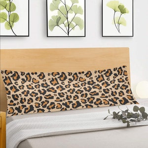 May include: A long, rectangular body pillow with a brown and black leopard print pattern. The pillow is on a bed with a white blanket and a wooden headboard.