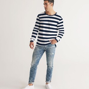 Op de afbeelding: Een persoon draagt een wit en donkerblauw gestreept shirt met lange mouwen, een blauwe jeans met distressed details en witte sneakers.