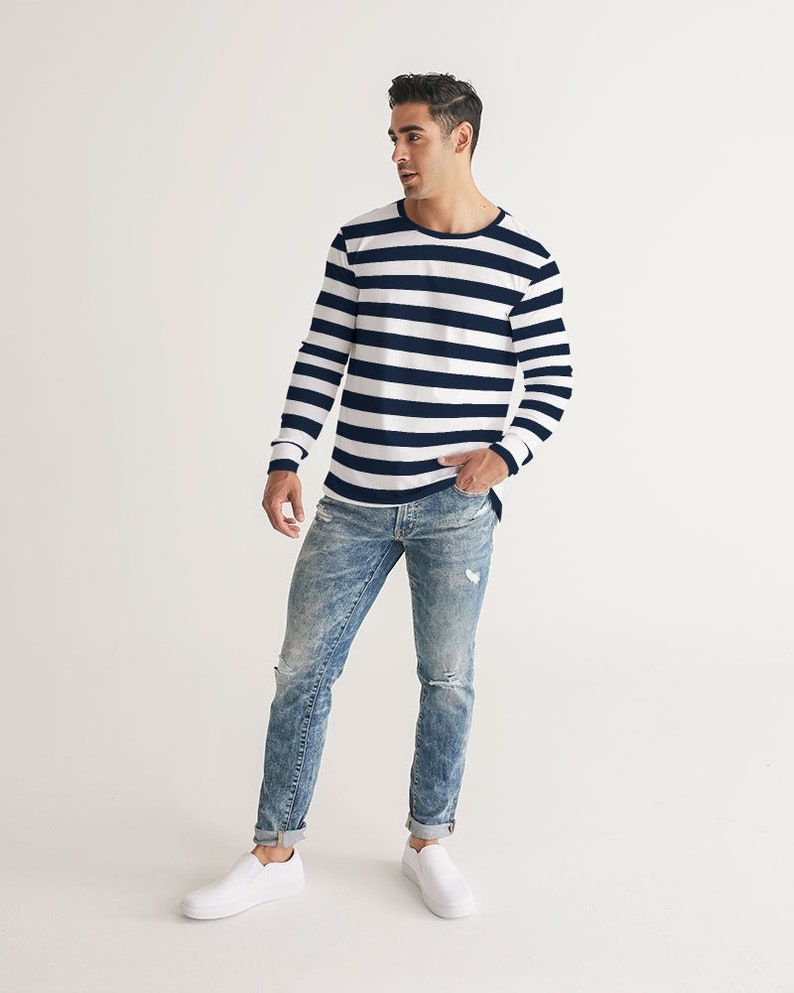 Op de afbeelding: Een persoon draagt een wit en donkerblauw gestreept shirt met lange mouwen, een blauwe jeans met distressed details en witte sneakers.