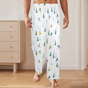 May include: White pajama trousers featuring a repeating pattern of skiers, evergreen trees, and blue snow-covered hills. The skiers wear various coloured outfits. The trousers are made of a soft, lightweight material.