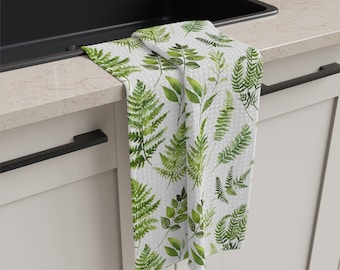 Puede incluir: Una toalla de cocina blanca con un patrón de helechos verdes. La toalla está colgada de un tirador de la puerta del armario.