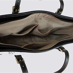 May include: Black leather tote bag with a zipper closure and a beige fabric lining. The bag has two interior pockets and two top handles.