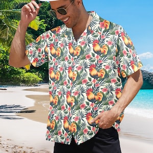 Puede incluir: Una camisa de manga corta con botones y estampado tropical con gallos, flores y hojas. La camisa es blanca con un estampado amarillo, naranja, rojo y verde.