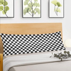 Könnte beinhalten: Ein schwarz-weiß kariertes Kissen mit weißem Hintergrund und schwarzen Quadraten. Das Kissen liegt auf einem Bett mit einer weißen Decke.