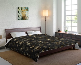 May include: A black and gold duvet cover with a celestial pattern featuring moons, stars, and suns. The duvet cover is on a bed with a wooden frame and white pillows.