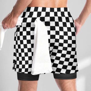 K&ouml;nnte beinhalten: Sportshorts mit schwarz-wei&szlig;em Karomuster und einer einfarbig schwarzen Innenschicht. Ein wei&szlig;es Handtuch ist in den Bund der Shorts gesteckt. Das Kleidungsst&uuml;ck hat einen breiten elastischen Bund und eine lockere Passform &uuml;ber dem Innenfutter.