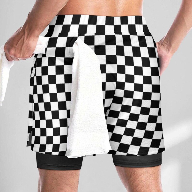 K&ouml;nnte beinhalten: Sportshorts mit schwarz-wei&szlig;em Karomuster und einer einfarbig schwarzen Innenschicht. Ein wei&szlig;es Handtuch ist in den Bund der Shorts gesteckt. Das Kleidungsst&uuml;ck hat einen breiten elastischen Bund und eine lockere Passform &uuml;ber dem Innenfutter.