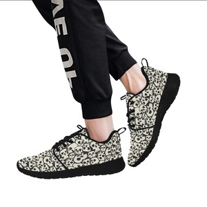 Pode incluir: Um par de tênis preto e branco com um padrão de caveira. Os tênis têm uma sola branca e uma parte superior preta com um padrão de caveira.