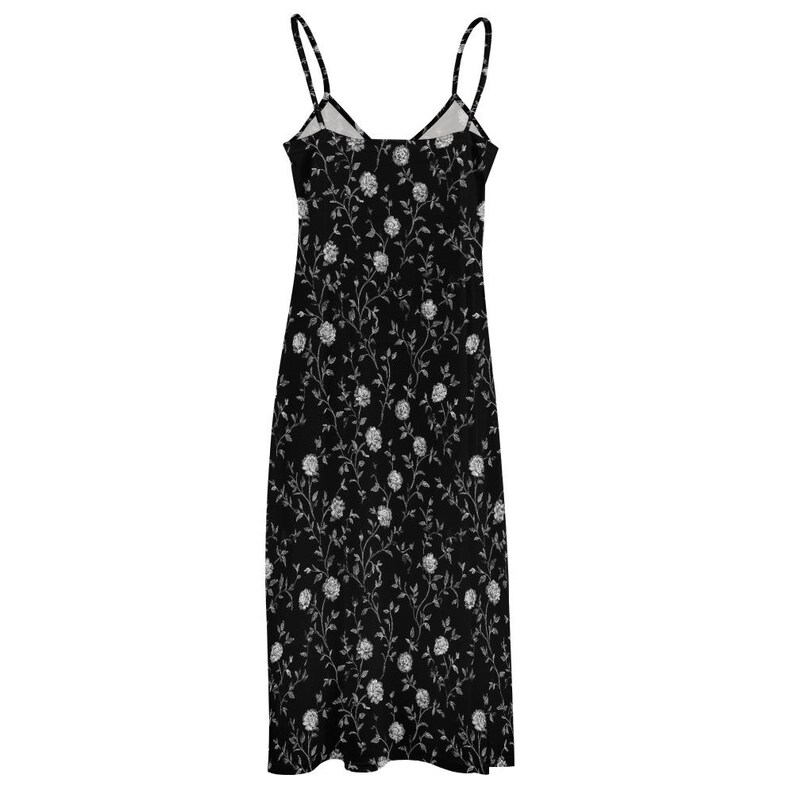 May include: A black midi dress with thin spaghetti straps. The dress is covered in a white floral pattern. The dress has a V-neckline and a straight, flowing silhouette. The dress is made of a lightweight fabric.