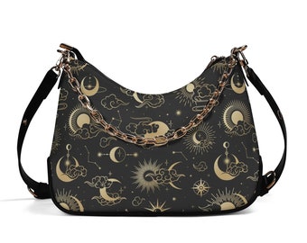 Puede incluir: Un bolso negro con una correa de cadena dorada y un estampado celestial con lunas, estrellas y nubes.