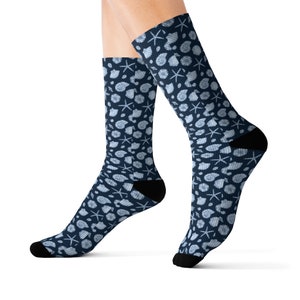 May include: A pair of blue socks with a white seashell and starfish pattern. The socks are made of a soft, comfortable material and are perfect for everyday wear.