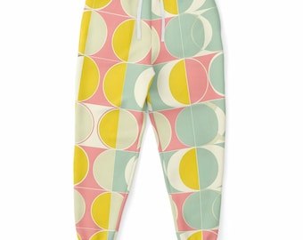 May include: Joggers featuring a repeating geometric pattern of circles and semicircles in shades of yellow, light blue, and pink on a cream background. The pants include a white drawstring at the elastic waistband and ribbed cuffs.