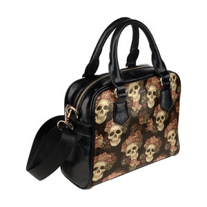 May include: A black faux leather handbag with a shoulder strap and top handles. The bag features a repeating pattern of white skulls with floral accents on a dark background.