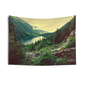 May include: A scenic view of a mountain lake surrounded by lush green trees and a waterfall cascading down a rocky hillside. The sky is a soft blue with wispy clouds.