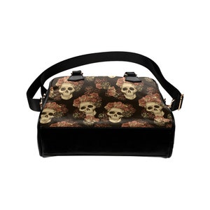 May include: A black leather handbag with a shoulder strap. The bag has a floral pattern with skulls and roses.