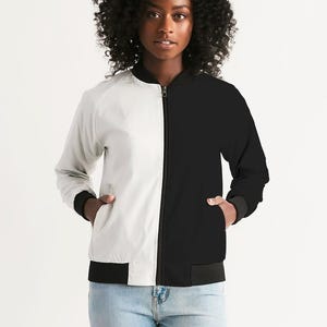 May include: A two-toned bomber jacket, split vertically with a white left side and a black right side. The jacket has a black collar, cuffs, and hem, with a full-length zipper. The model is wearing blue jeans.