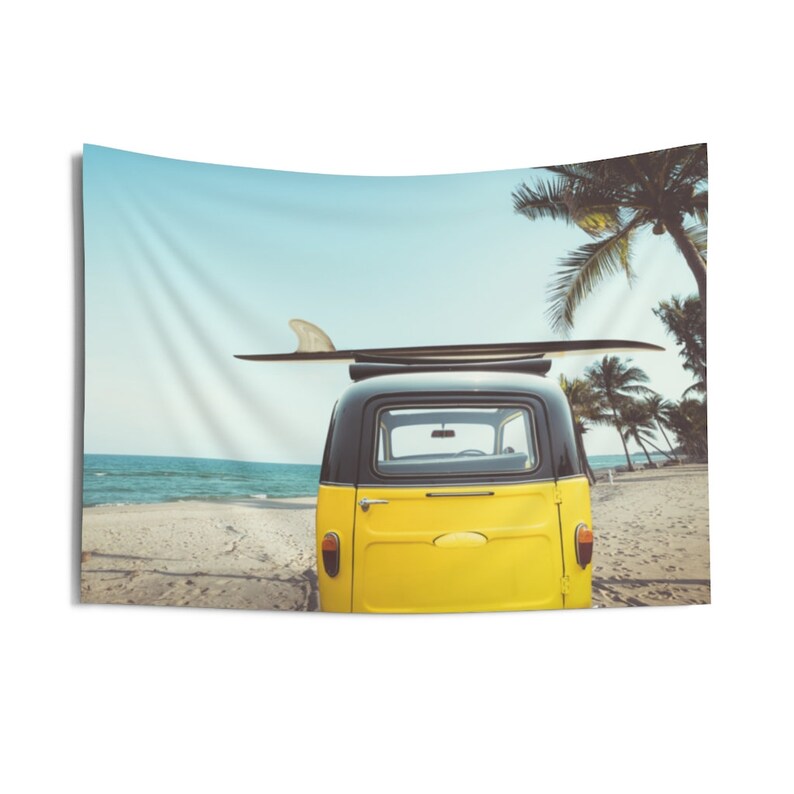 May include: A yellow vintage van with a black roof and a surfboard on top parked on a sandy beach with palm trees in the background.