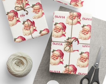 May include: Christmas-themed gift wrap featuring a repeating pattern of Santa Claus faces in red and white. The wrapped gifts are tied with twine and include small tags. A spool of twine, scissors, and blank tags are also visible.