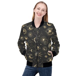 Puede incluir: Una chaqueta bomber negra con un patrón celestial dorado con lunas, estrellas y nubes.