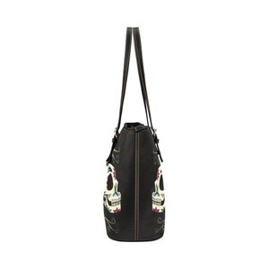 May include: Black tote bag with two sugar skull designs on the front. The skulls are white with colorful floral details.