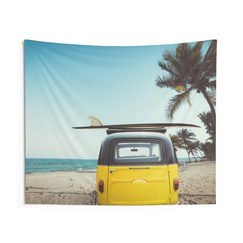 May include: A yellow vintage van with a black roof and a surfboard on top, parked on a sandy beach with palm trees in the background.