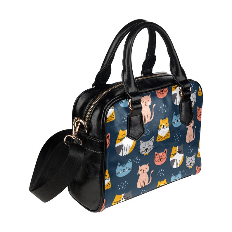 May include: A black leather handbag with a shoulder strap and top handles. The bag features a colorful print of cartoon cats on a dark blue background.