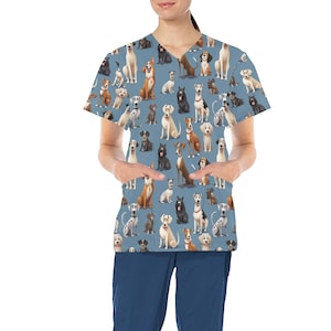 Puede incluir: Una blusa azul con un estampado de varias razas de perros. La blusa tiene cuello en V y dos bolsillos delanteros. Los perros están representados en varias poses y colores, incluyendo marrón, negro, blanco y beige.