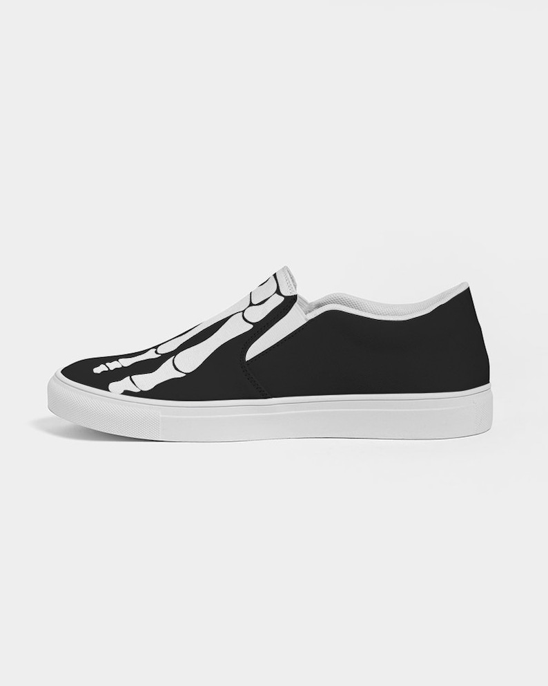 May include: Black slip-on canvas shoes with a white skeleton design on the upper. The shoes have a white rubber sole.