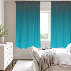 Könnte beinhalten: Zwei tealfarbene Ombre-Vorhänge hängen vor einem Fenster. Die Vorhänge gehen von einem dunklen Teal oben zu einem hellen Teal unten über. Die Vorhänge hängen in einem Schlafzimmer mit einer weißen Kommode und einem Bett.