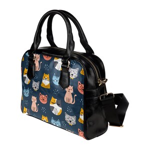 May include: A black leather handbag with a shoulder strap and a colorful cat print. The print features cats of different colors and patterns on a blue background.