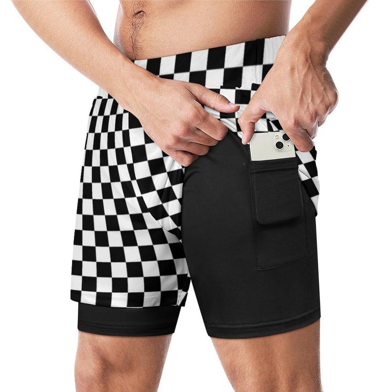 K&ouml;nnte beinhalten: Sportshorts mit schwarz-wei&szlig;em Schachbrettmuster und integrierter schwarzer Kompressionsschicht. Die Shorts haben eine Tasche auf der rechten Seite, die ein wei&szlig;es Smartphone h&auml;lt. Die &auml;u&szlig;ere Schicht zeigt ein auff&auml;lliges Schachbrettmuster.
