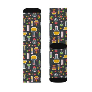 May include: A pair of black socks with a colorful pattern of beakers, flasks, and other science-related imagery. The socks are designed for adults.